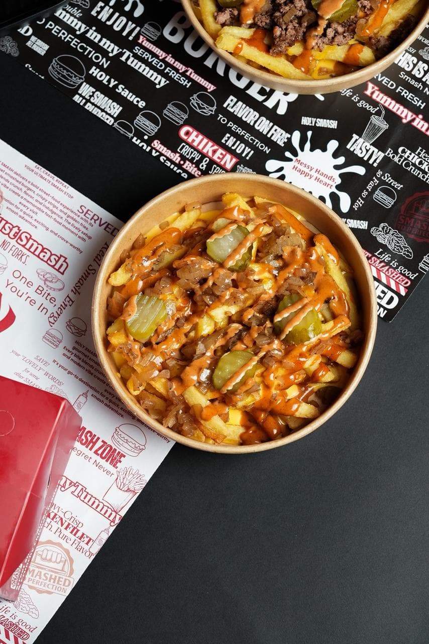 Bowl of loaded smash fries with pickles and sauce drizzle